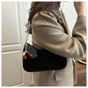 Detail of black suede hobo bag with gold metal chain strap and red cherry charm