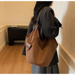 Brown suede tote bag with long strap and detachable charm shown in cozy room
