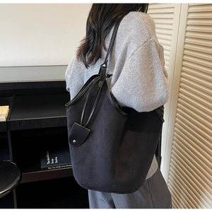 Detail of minimalist black large tote bag with leather pendant strap on a shoulder