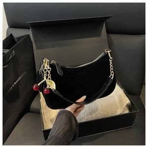 Detail of black hobo bag with gold chain and cherry charm in luxury gift packaging