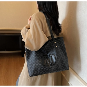 Detail of a black patterned tote bag with M-letter print and embossed gold emblem