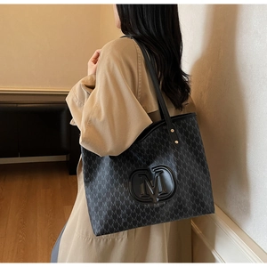 Detail of large black tote bag with M patterns on beige trench coat for commuters