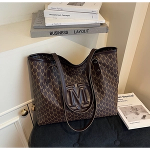 Close-up of brown tote bag with M-letter monogram print and textured leather finish