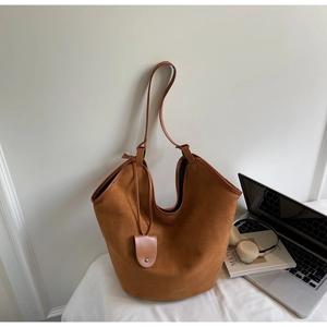 Detail of tan suede tote bag with leather straps and charm against casual office props