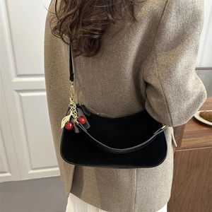 Minimalist black velvet hobo bag with red cherry charm shown on model in a chic indoor setting