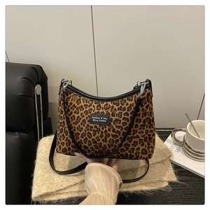 Dettaglio della borsa tote leopardata con manici neri e patch logo su sfondo divano