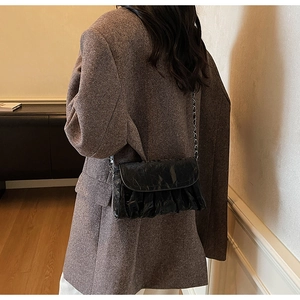 Détail d'un sac à bandoulière noir brillant plissé porté par un mannequin en scène