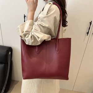 Chic burgundy leather tote bag with long shoulder straps shown on a model in a studio