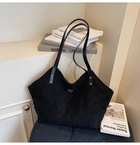 Close-up of black quilted tote bag featuring a metal logo and textured suede finish