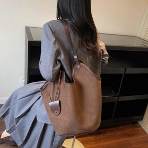 Brown matte leather tote bag with small pouch shown on model in a modern interior setting