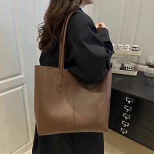 Minimalist brown leather tote bag with large capacity shown on model in black coat