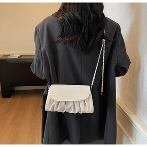 Détail du sac bandoulière blanc crème plissé avec chaîne argentée porté par le mannequin