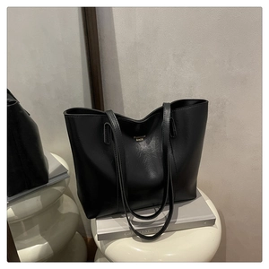 Vue détaillée du sac cabas noir texturé avec lettrage doré sur un piédestal minimaliste