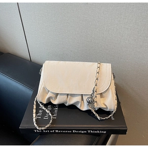 Détail du sac plissé crème avec chaîne argentée et breloque sphère sur un livre