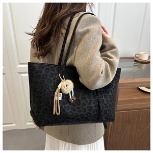 Gros plan du sac cabas noir à motif léopard avec un pendentif en peluche doux