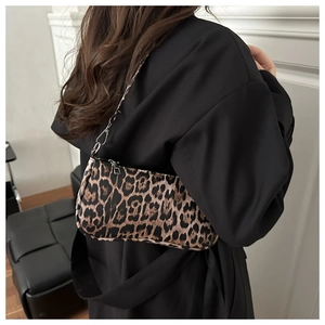 Leopard print underarm bag with metal chain detail shown on shoulder in a lifestyle setting