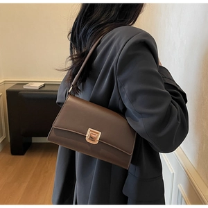 Detail of a brown leather baguette bag with a gold rectangular buckle on a grey suit