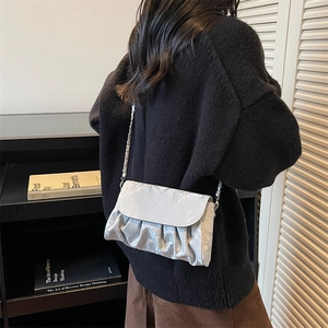 Sac bandoulière plissé argenté avec chaîne porté par un mannequin dans une pièce moderne