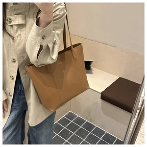 Detail view of camel leather tote bag with logo and slim shoulder straps on model