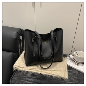 Detail of black matte leather tote bag with gold logo lettering on a chic desk setup