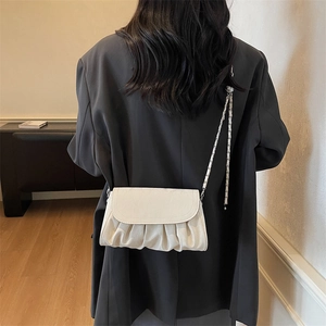 Sac bandoulière plissé blanc cassé avec chaîne argentée porté sur un blazer gris