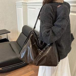 Deep brown leather tote bag with vintage metal buckle shown on shoulder of a model