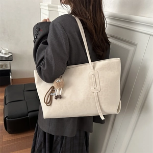 Sac cabas crème à motif léopard avec breloque en peluche porté par un mannequin chic