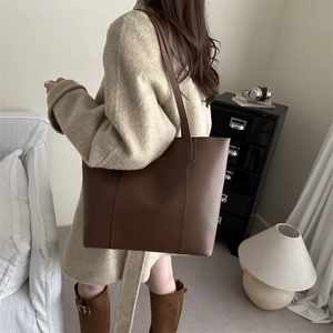 Minimalist brown leather tote bag carried by model in a stylish wool coat and boots