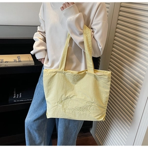 Detail of pale yellow tote bag featuring heart embroidery and crinkled nylon texture