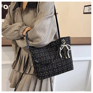 Details einer Tweed-Tragetasche mit Perlen-Schleifen-Anhänger an einem weiblichen Model