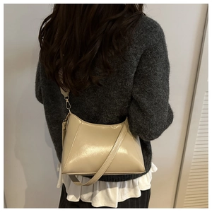 Détail du sac bandoulière en cuir verni crème avec large sangle sur un pull gris