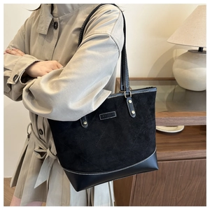 Detail of black quilted tote bag with suede texture and fashion metal plaque on front