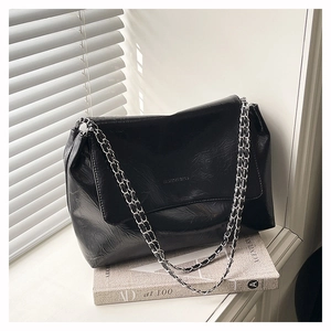 Detail of glossy black wrinkled leather shoulder bag with silver chain and embossed text