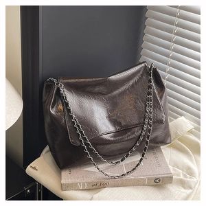 Macro detail of dark brown wrinkled leather texture and silver chain strap on a tote bag