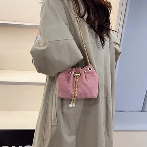 Sac seau en velours rose avec chaîne dorée et cordon perlé sur fond de manteau beige