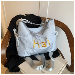 Detail of silver nylon tote bag with gold Hai embroidery and side ribbon bow decoration