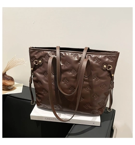 Detail of dark brown tote bag featuring embossed bow patterns and golden metal hardware