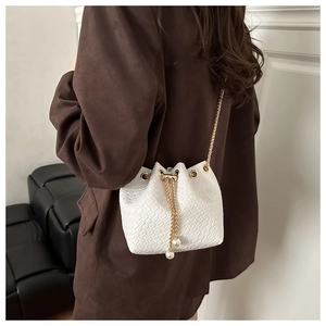 Detail of white crocodile pattern bucket bag with gold chain and pearl drawstring