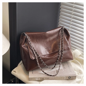 Detail of a brown pleated tote bag featuring silver chain straps and embossed lettering