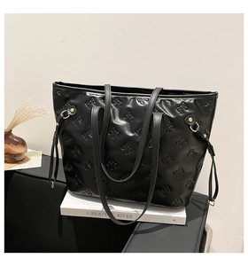 Detail of black tote bag with embossed bow patterns on glossy synthetic leather
