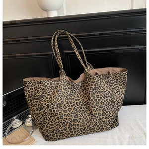 Detail of a large leopard print canvas tote bag on a bed next to a laptop and headphones