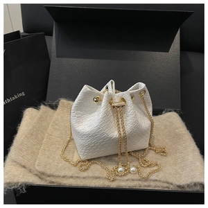 Close-up of white woven bucket bag with gold chain strap and pearl drawstring detail