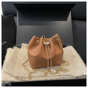 Detail of brown woven bucket bag with gold chain strap and pearl accents in a gift box