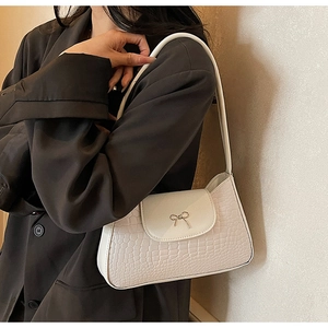 Detail of a chic cream white croc-effect shoulder bag with a metal bow decoration