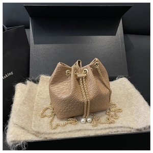 Detail of beige textured bucket bag with gold chain and pearl drawstring in a luxury gift box