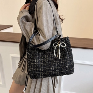 Sac bandoulière élégant en tweed noir avec détails dorés et breloque perle sur modèle