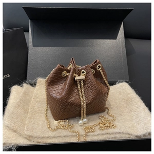 Detail of brown woven bucket bag with pearl drawstring and gold chain strap in a gift box