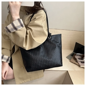 Detail of a large black woven leather tote bag with round handles for autumn and winter