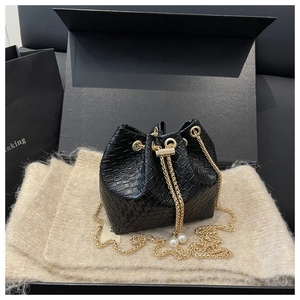 Close-up of woven bucket bag featuring gold chain strap and elegant pearl charm detail