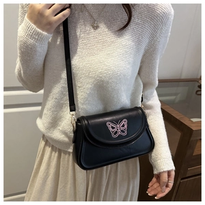 Detail of pink butterfly embroidery on a black faux leather crossbody bag worn by a model